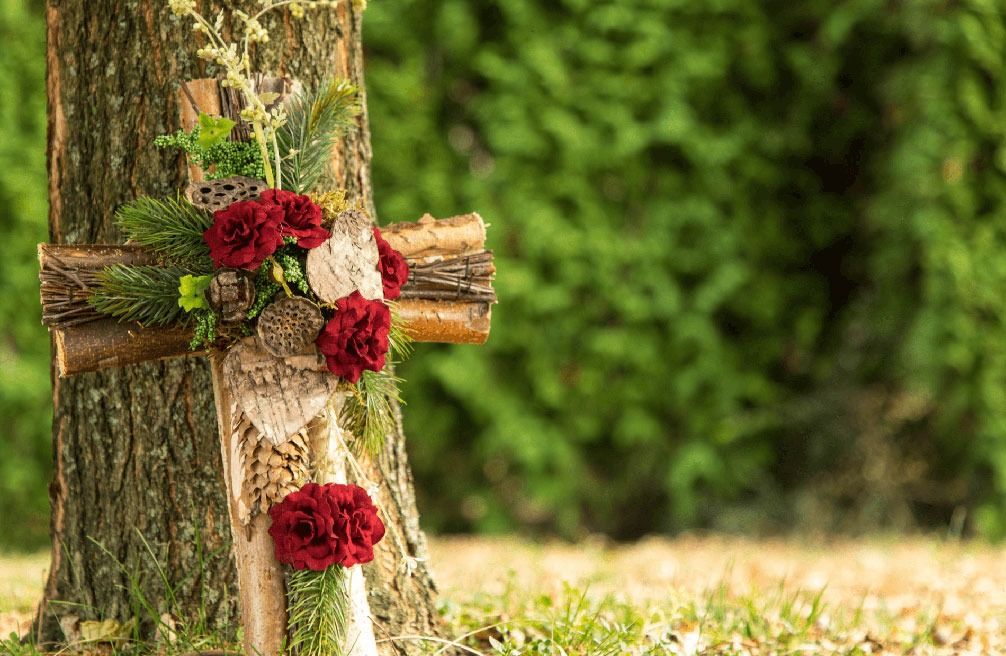 wooden cross decorated with flowers kept need the tree